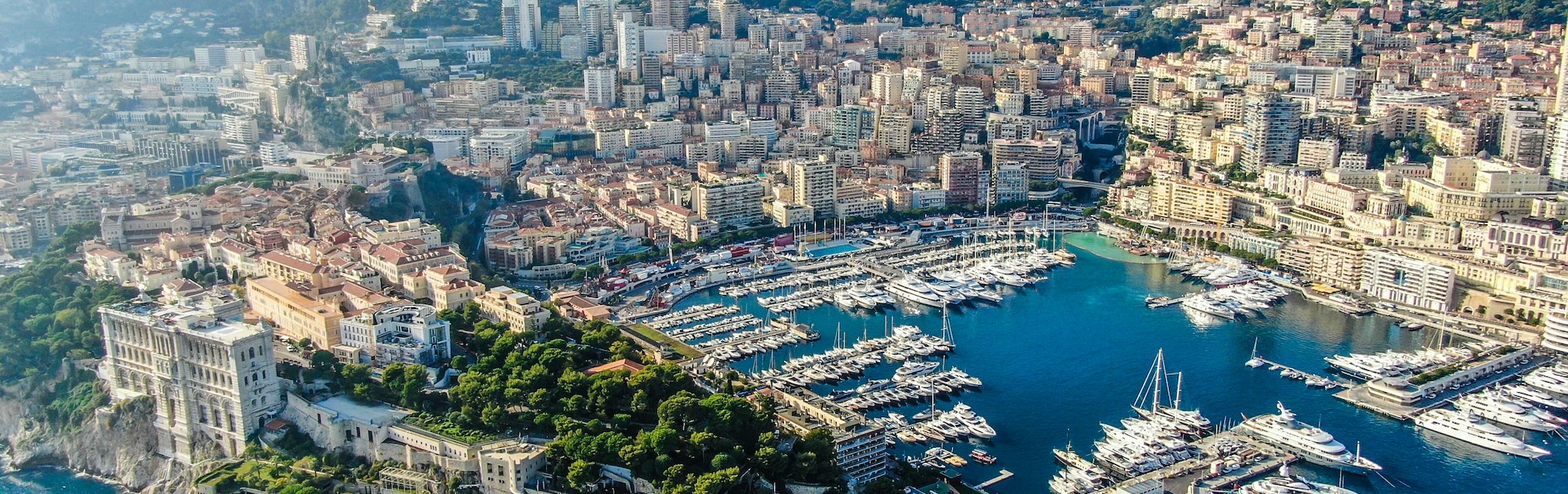 Drone perspective of Port Hercule and the Monaco skyline, showcasing superyachts and the prestigious Riviera setting.